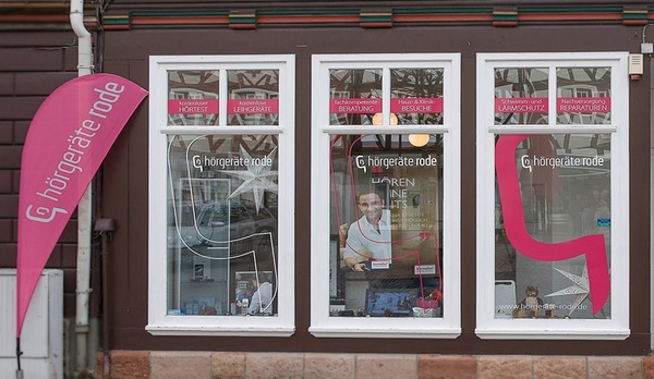 Fassade eines Hörgeräte-Fachgeschäfts mit Schaufenstern und Werbebanner in Pink.